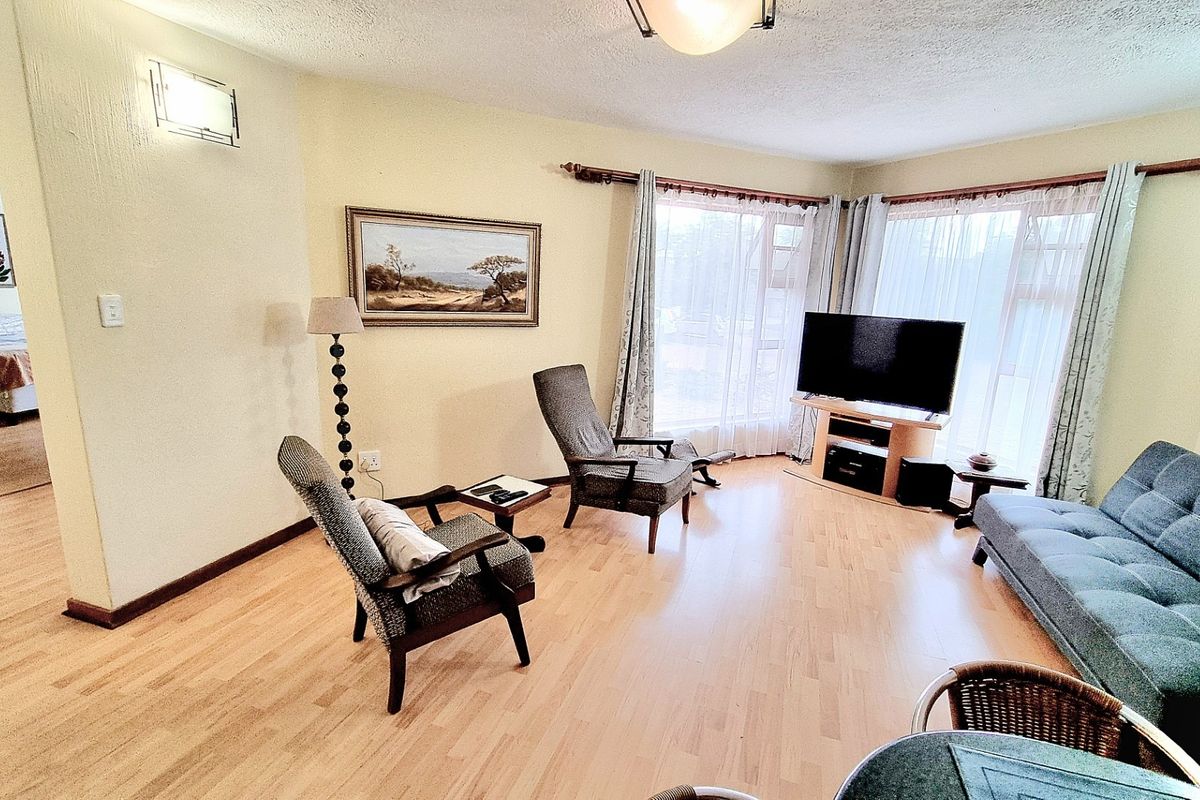 A bright living room featuring laminate flooring, large windows allowing natural light, and neutral wall finishes.
