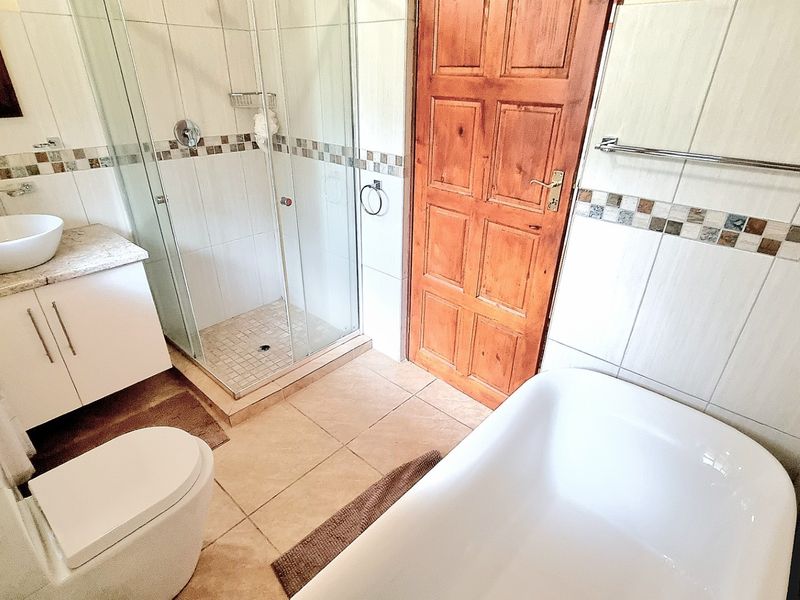 A functional bathroom featuring a glass-enclosed shower, a freestanding bathtub, a modern vessel sink on a vanity cabinet, and neutral wall tiling.