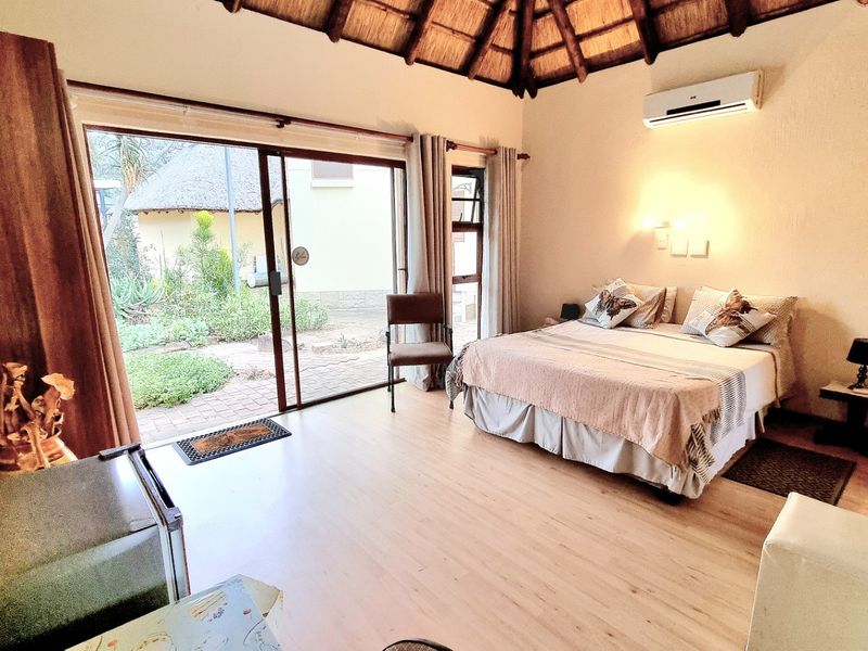 A spacious bedroom featuring a high thatched ceiling, laminate flooring, and a sliding glass door providing direct access to the garden.