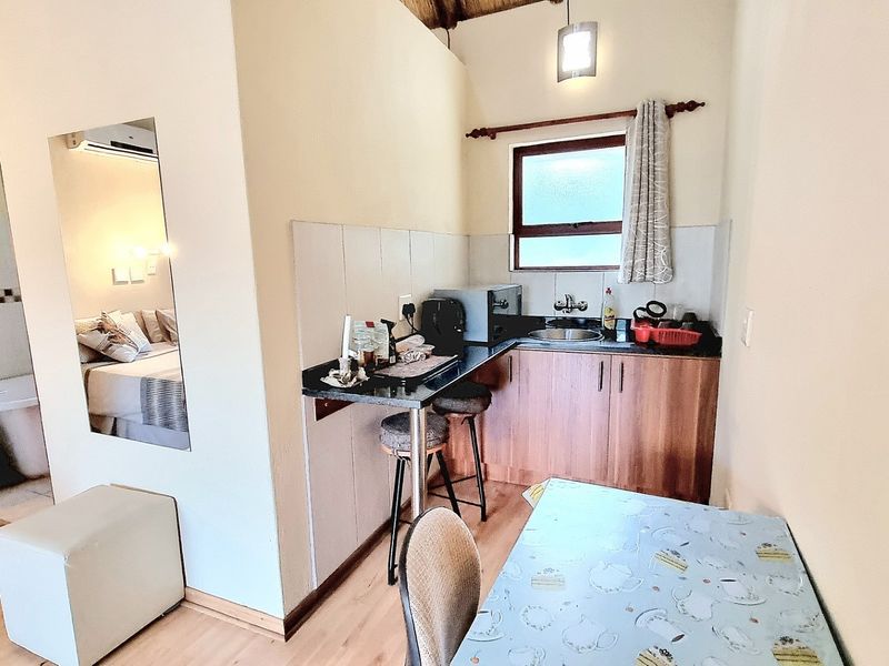 Compact kitchenette featuring built-in cabinetry, laminate countertops, a stainless steel sink, and tiled splashback, with adjacent access to a bedroom area.