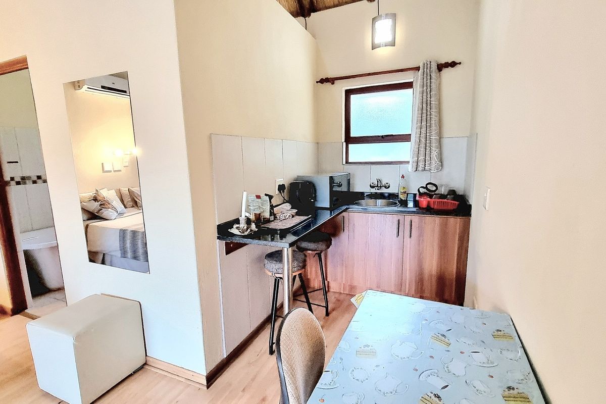 Compact kitchenette featuring built-in cabinetry, laminate countertops, a stainless steel sink, and tiled splashback, with adjacent access to a bedroom area.