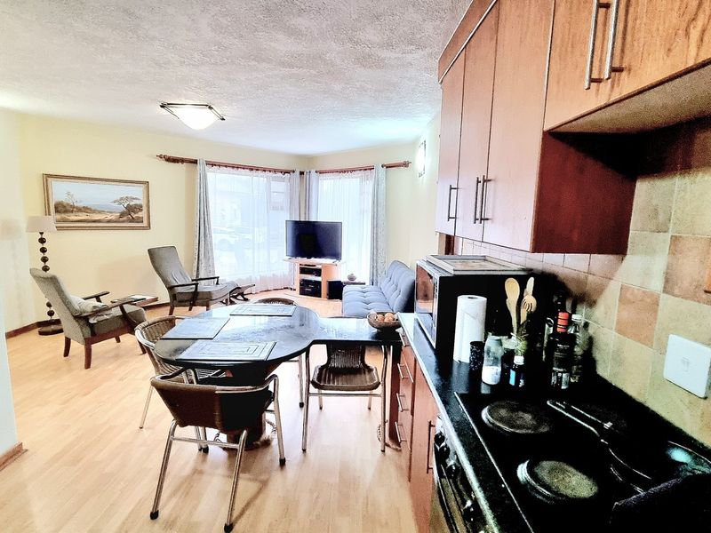 Open-plan living and kitchen area featuring laminate flooring, wooden cabinetry, and an electric hob, creating a functional combined space.