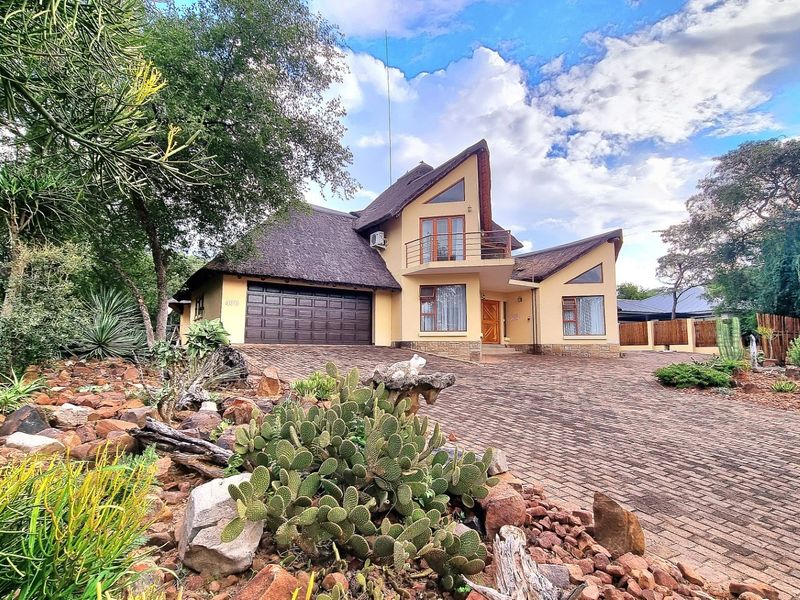 A well-maintained double-story home featuring a distinctive thatched roof, stone accents, a paved driveway, and an integrated double garage.