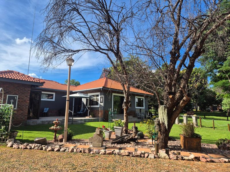 A well-maintained rear exterior view of the house featuring a terracotta tiled roof, brick masonry, and a landscaped garden with a paved patio area.