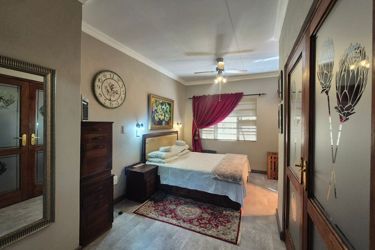 A well-maintained bedroom featuring tiled flooring, coved cornicing, a ceiling fan, and decorative frosted glass panel doors.