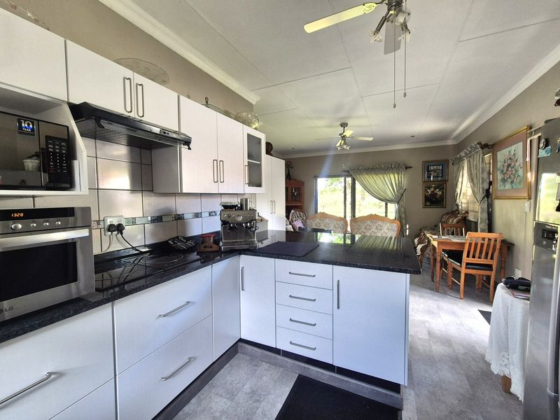 Open-plan kitchen and dining area featuring modern white cabinetry, granite countertops, built-in appliances, and direct access to the outdoor space via sliding doors.