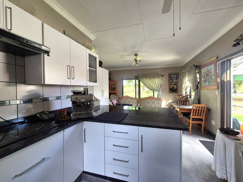 Open-plan kitchen featuring white cabinetry, granite countertops, and an integrated hob, flowing into a living and dining area with access to the outdoors.