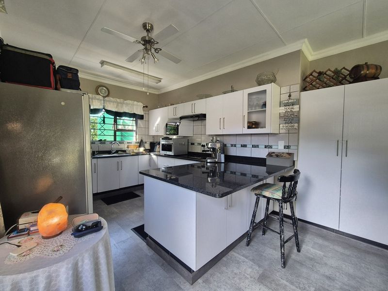 A functional kitchen featuring white cabinetry, granite countertops, a tiled backsplash, and a central island with breakfast bar seating.