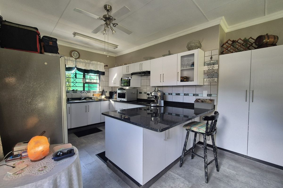 A functional kitchen featuring white cabinetry, granite countertops, a tiled backsplash, and a central island with breakfast bar seating.