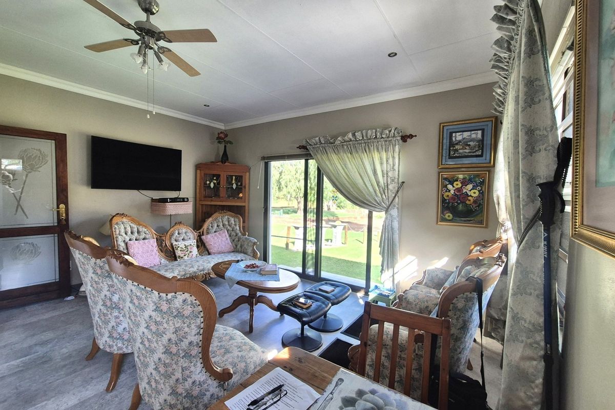 A comfortable living room featuring laminate flooring, a ceiling fan, and large sliding glass doors that provide natural light and access to the garden.
