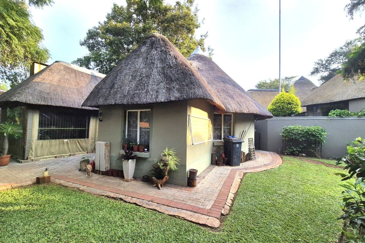 Rear view of a property featuring a traditional thatch roof, paved patio area, and established garden surroundings.