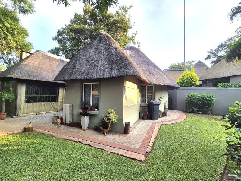 Rear view of a property featuring a traditional thatch roof, paved patio area, and established garden surroundings.