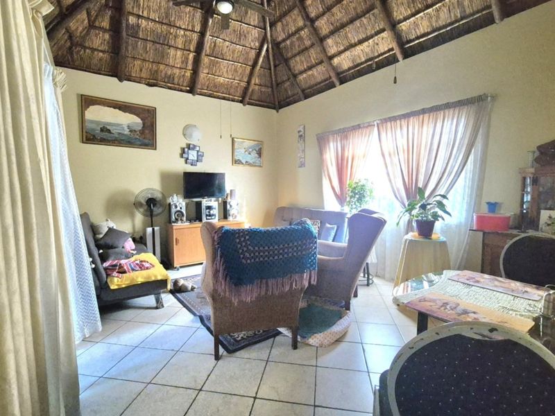 A living room featuring a traditional thatched roof with exposed timber rafters and ceramic floor tiles.