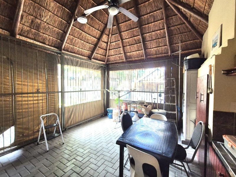 Covered outdoor patio area featuring a traditional thatched roof, paved flooring, and secure enclosure, offering a versatile space for outdoor living and entertaining.