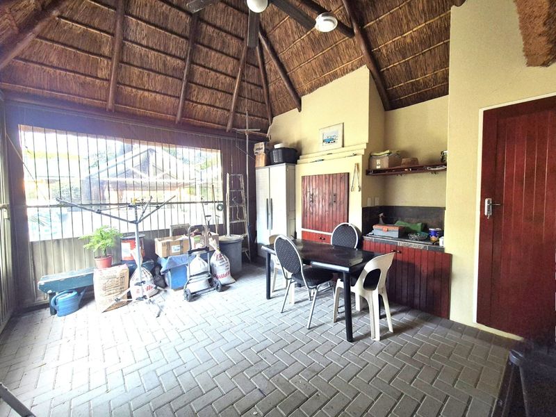 Covered patio area featuring a traditional thatched roof, exposed timber rafters, built-in cabinetry with a tiled countertop, and durable paved flooring.