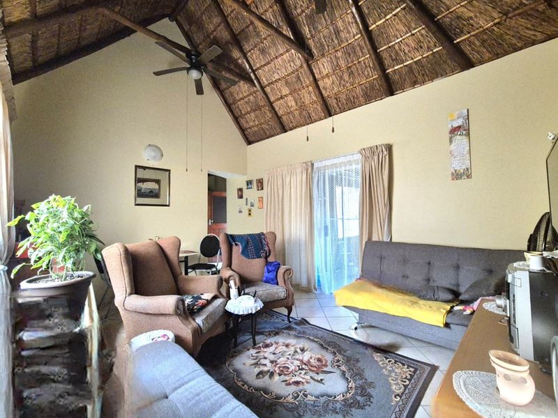 Living room featuring a high vaulted thatched ceiling with exposed timber rafters, tiled flooring, and a sliding glass door providing access to the outdoors.