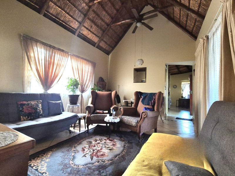 A cozy living room featuring a high vaulted thatched ceiling, a ceiling fan, and tiled flooring, creating a warm and rustic atmosphere.