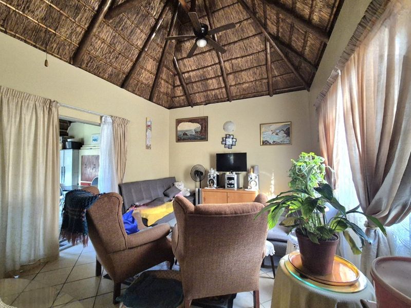 A cozy living room featuring a high vaulted thatched ceiling with exposed timber rafters, a ceiling fan, and tiled flooring.
