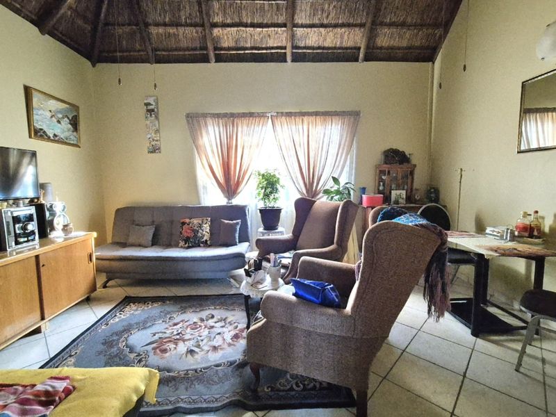 A living room featuring a traditional thatched roof with exposed timber rafters and tiled flooring, offering a rustic aesthetic.