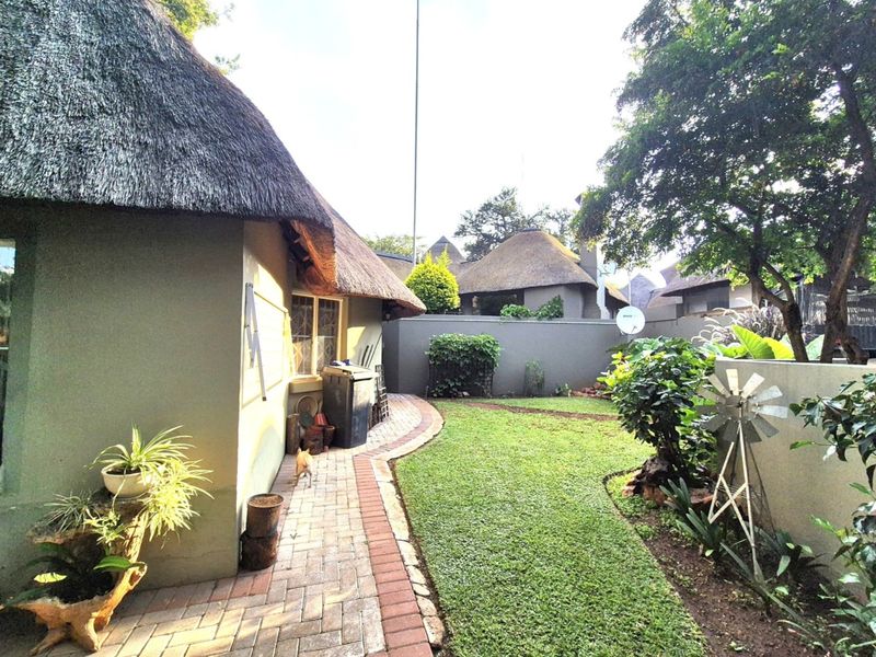 A rear garden view featuring a thatched roof dwelling, a brick-paved pathway, and a well-maintained lawn enclosed by a boundary wall.