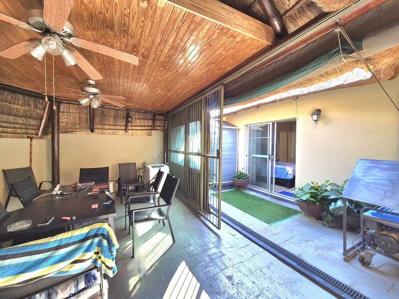 A covered patio area featuring a thatched roof, timber ceiling, ceiling fans, and paved flooring, providing a functional outdoor entertainment space.