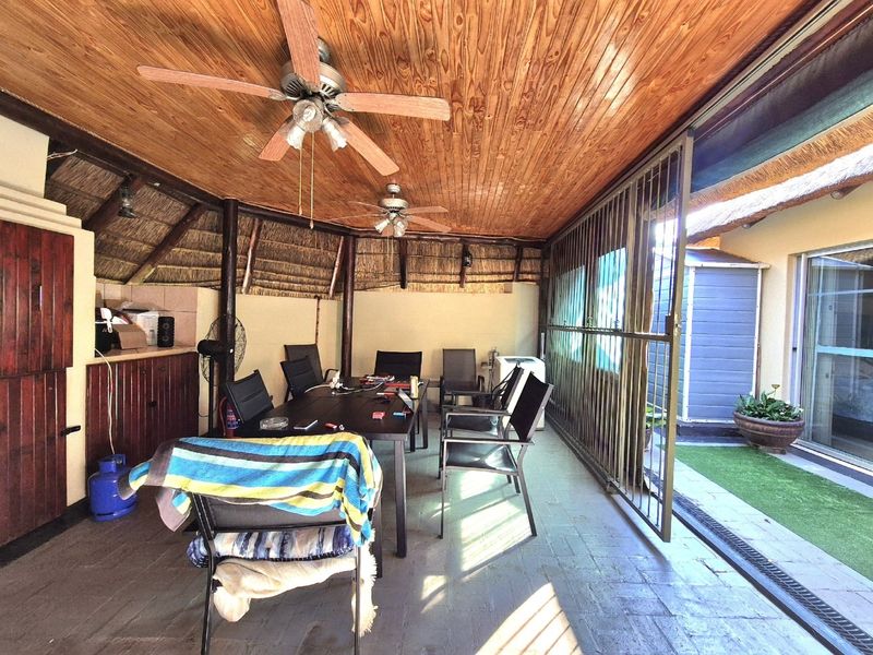 Covered patio area featuring a timber ceiling, thatch roofing, ceiling fans, and built-in cabinetry, providing a functional outdoor entertainment space.