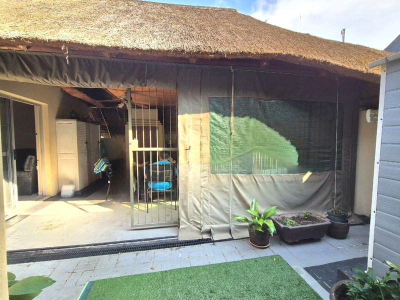 Covered patio area featuring a traditional thatch roof, paved flooring, and protective canvas drop-down blinds, providing a sheltered outdoor living space.
