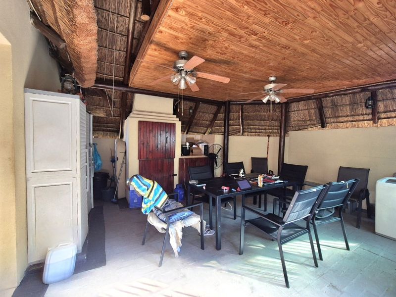 Covered outdoor patio area featuring a traditional thatch roof, timber ceiling, ceiling fans, and a built-in braai, ideal for outdoor entertaining.