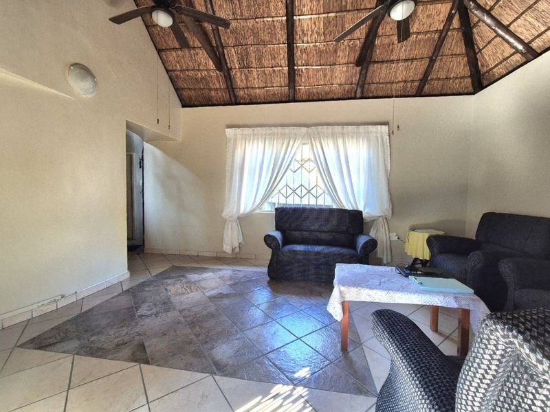 Spacious living room featuring a high thatched ceiling with exposed timber rafters, ceiling fans, and tiled flooring.