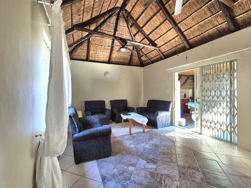 Spacious living area featuring a high vaulted thatched roof with exposed timber rafters, ceiling fan, and durable tiled flooring with access to an outdoor area.