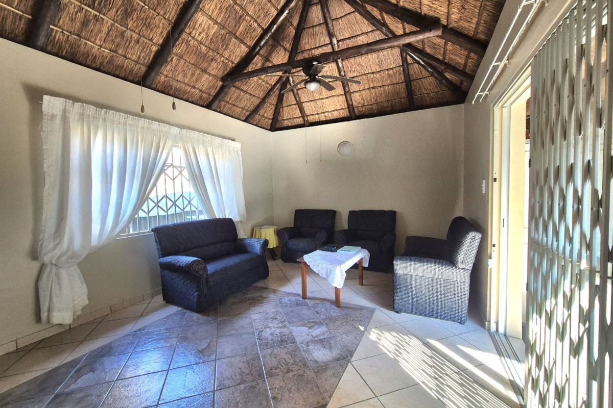A living room featuring a traditional thatched roof with exposed timber beams, tiled flooring, and a ceiling fan, providing a rustic and spacious atmosphere.
