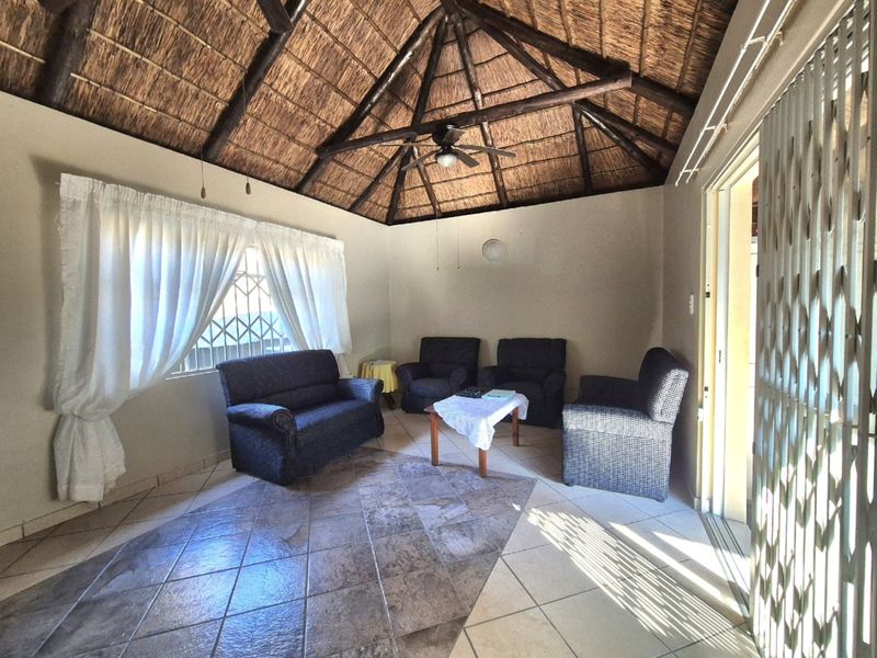 A living room featuring a traditional thatched roof with exposed timber beams, tiled flooring, and a ceiling fan, providing a rustic and spacious atmosphere.