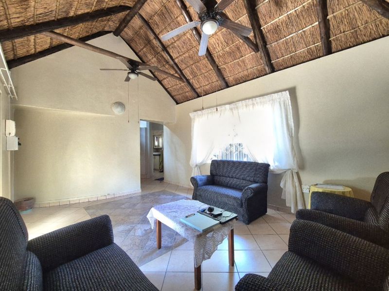Spacious living room featuring a high vaulted thatched ceiling with exposed timber beams, ceiling fans, and neutral tiled flooring.