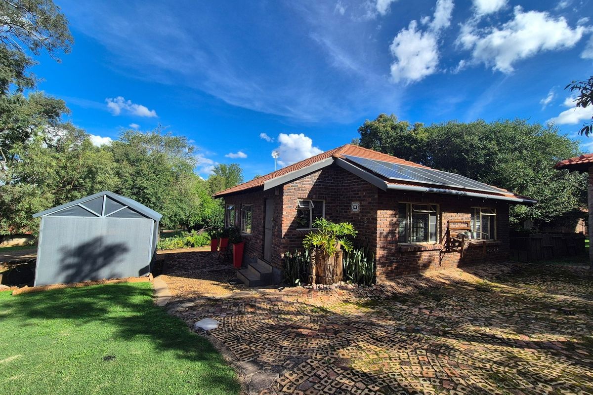 Rear view of a face brick house featuring a tiled roof with solar panels, a paved driveway, and a detached metal garden shed.