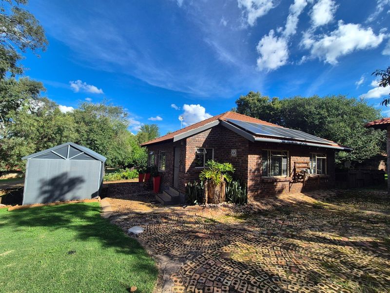 Rear view of a face brick house featuring a tiled roof with solar panels, a paved driveway, and a detached metal garden shed.