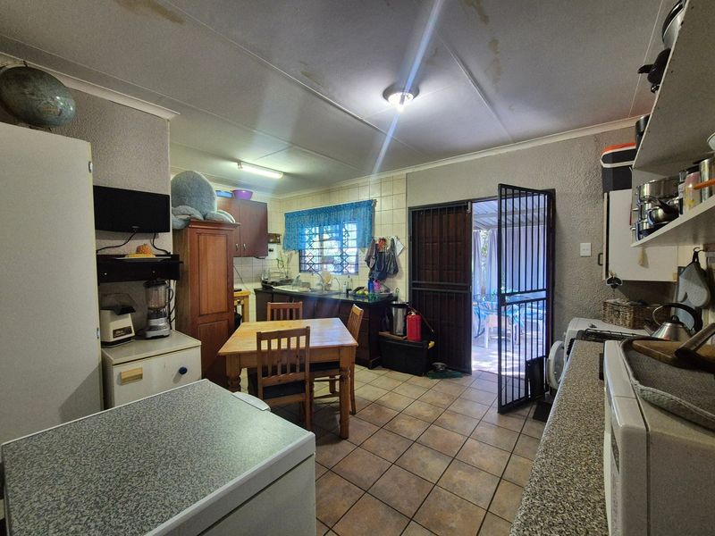 A functional kitchen area featuring tiled floors, laminate countertops, and direct access to an outdoor patio through a security gate.