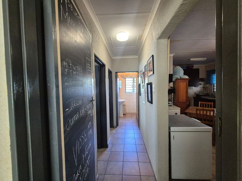 A functional hallway featuring tiled flooring and access to adjacent rooms, including a view into the kitchen and a bathroom at the end.