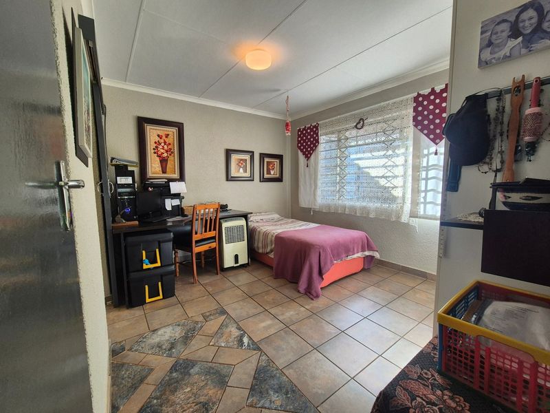 A functional bedroom featuring tiled flooring, a window with security bars, and a drop ceiling, offering a practical space for rest or study.