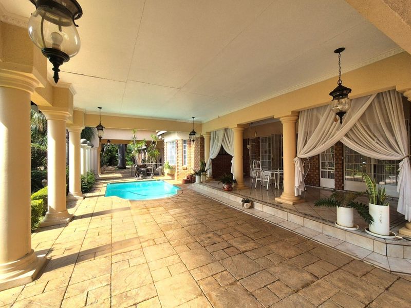 Spacious covered patio featuring paved flooring, classic columns, and direct access to an integrated swimming pool, ideal for outdoor entertaining.