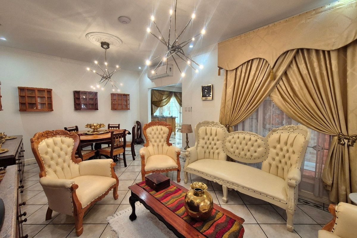 A spacious living room featuring tiled flooring, decorative ceiling roses with modern chandeliers, and wall-mounted air conditioning, offering a comfortable and well-lit living space.