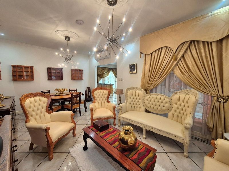 A spacious living room featuring tiled flooring, decorative ceiling roses with modern chandeliers, and wall-mounted air conditioning, offering a comfortable and well-lit living space.