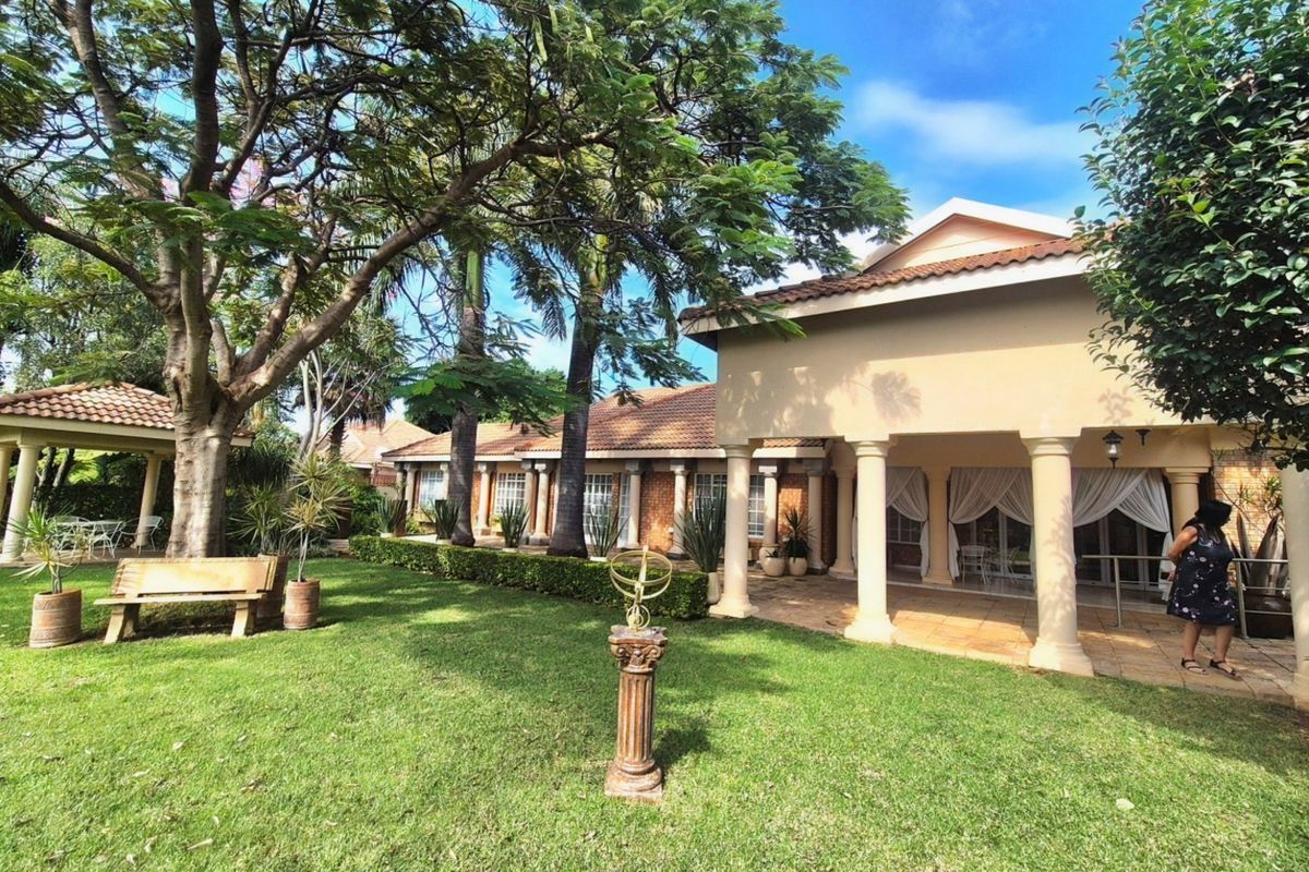Spacious rear garden featuring a covered patio with classical columns, a tiled roof, and a separate gazebo, offering a serene outdoor living space.