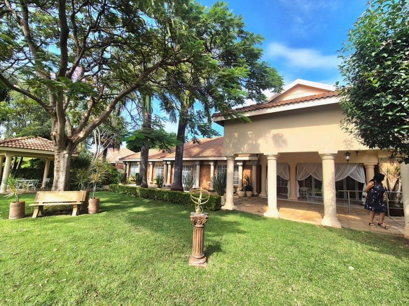 Spacious rear garden featuring a covered patio with classical columns, a tiled roof, and a separate gazebo, offering a serene outdoor living space.