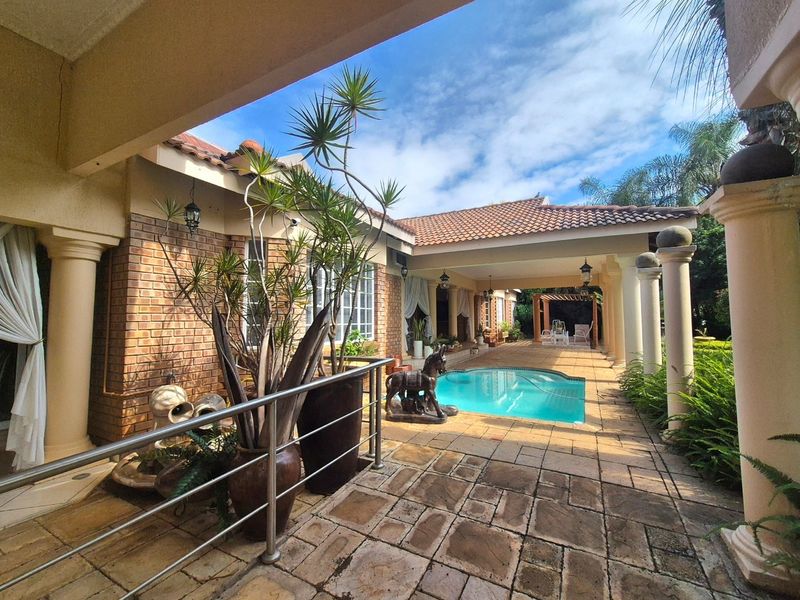 A spacious outdoor entertainment area featuring a swimming pool, covered patio with classic columns, and durable stone paving, perfect for relaxed outdoor living.