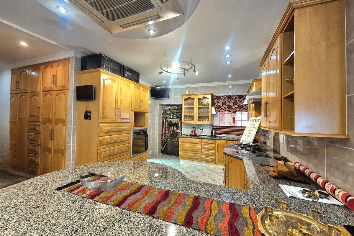 Spacious kitchen featuring extensive wooden cabinetry, granite countertops, built-in oven, gas hob, and integrated ceiling air conditioning.