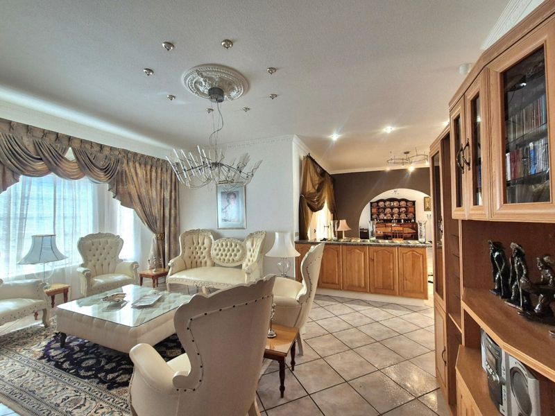 Spacious open-plan living area featuring tiled flooring, decorative ceiling details, and a transition into a dining space through a classic archway.