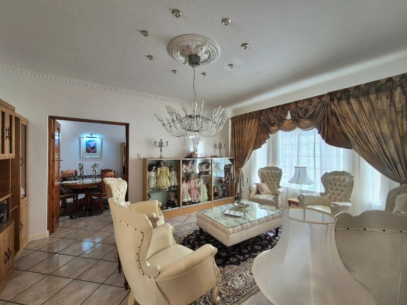 A formal living room featuring decorative ceiling cornicing, a central ceiling rose, recessed lighting, and tiled flooring, with an open transition to the dining area.