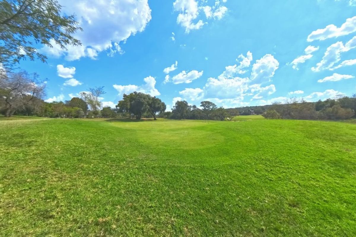 A wide-angle view of a spacious, well-maintained grassy residential plot featuring mature trees and open landscape.
