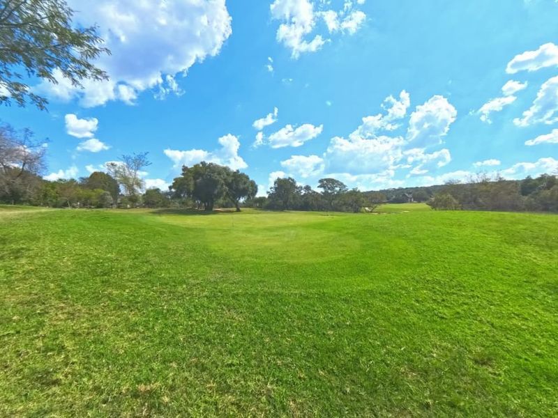 A wide-angle view of a spacious, well-maintained grassy residential plot featuring mature trees and open landscape.