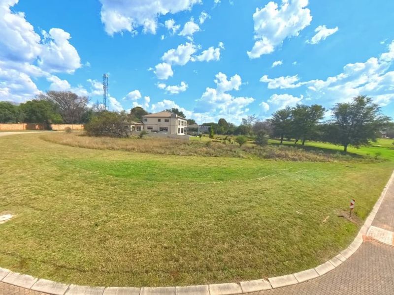A wide-angle view of a vacant residential plot featuring a manicured grass lawn, paved road access, and established perimeter curbing.
